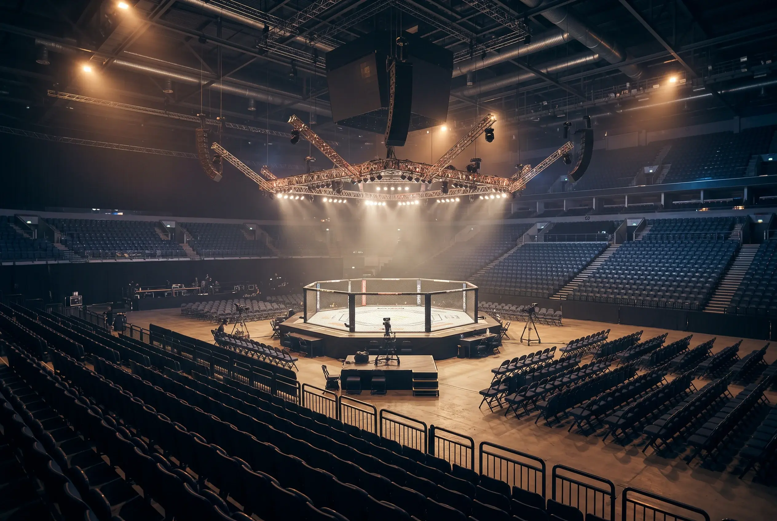 UK arena interior with the UFC octagon set up before fight night, empty spectator seats lit warmly